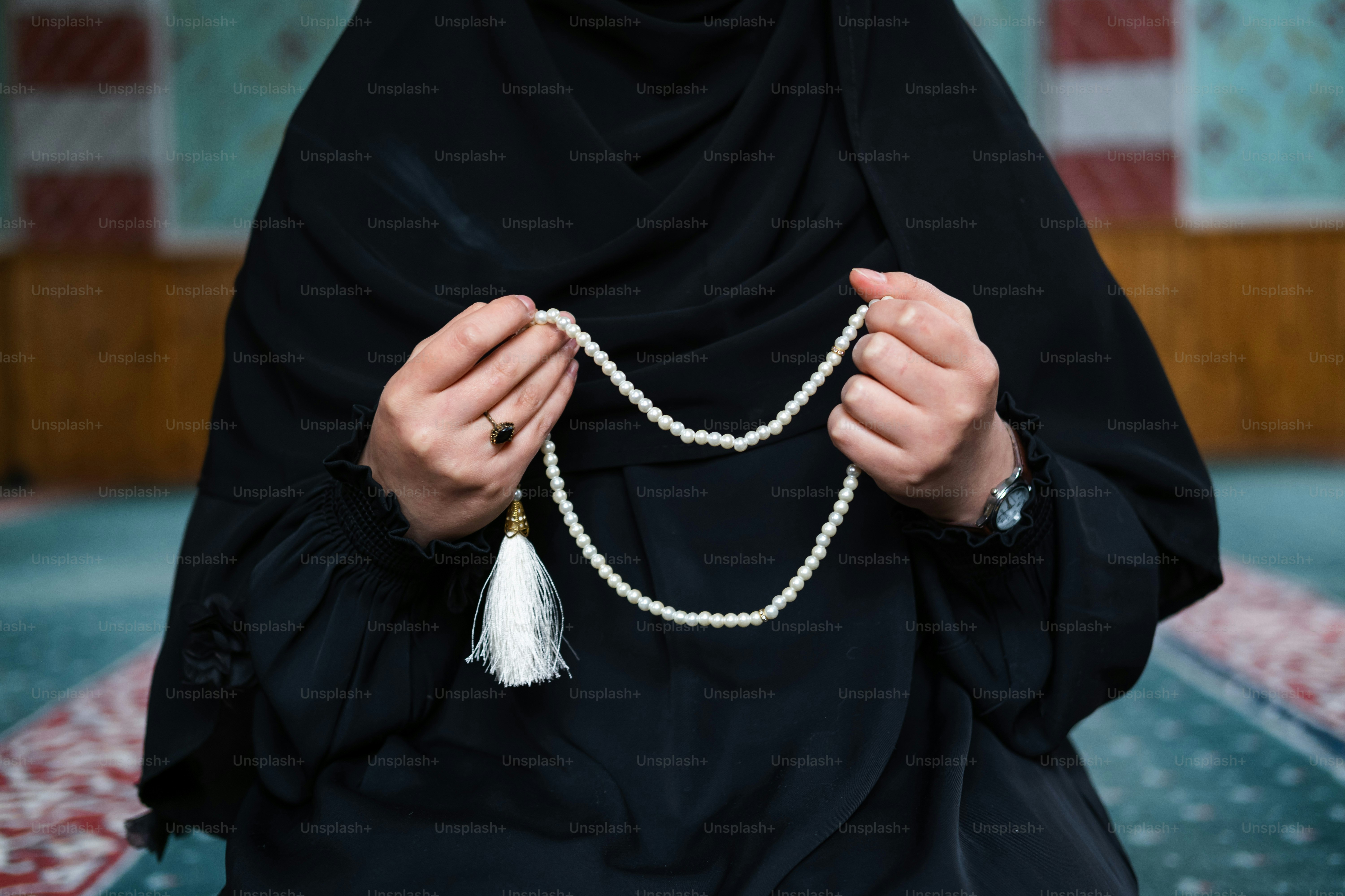 a woman wearing a black hijab holding a white beaded necklace