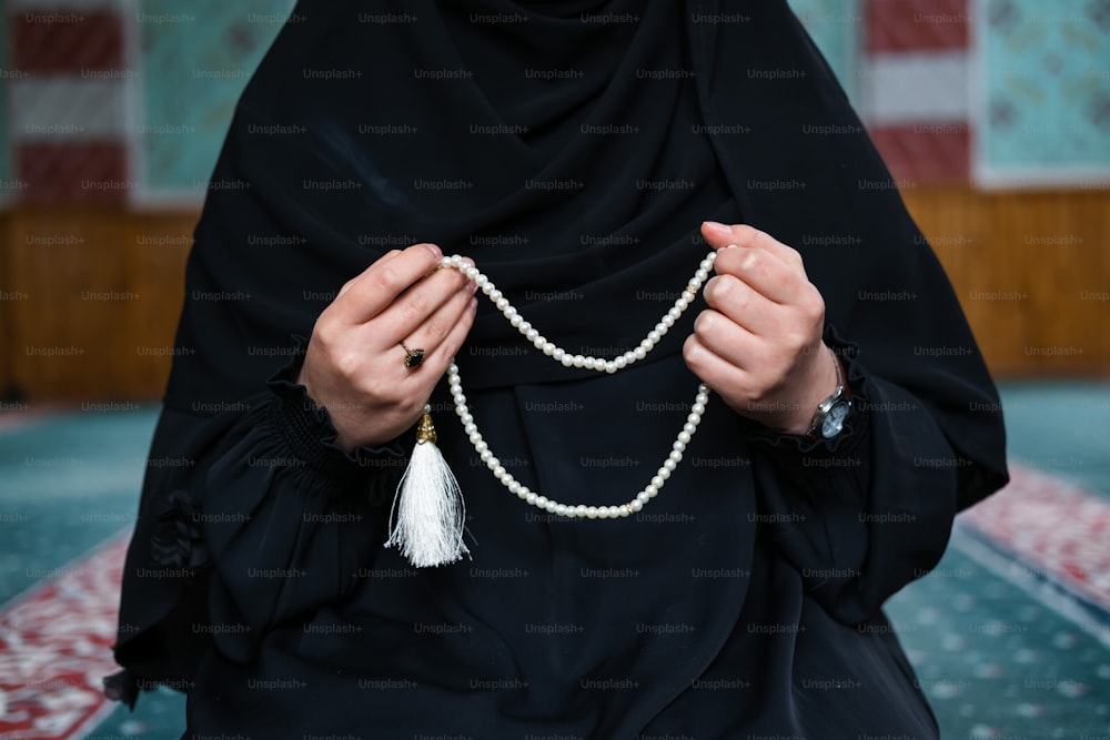 a woman wearing a black hijab holding a white beaded necklace
