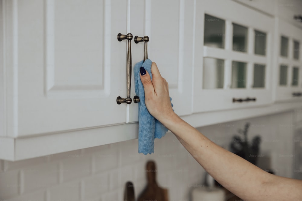 uma mulher que limpa um armário de cozinha com uma toalha azul