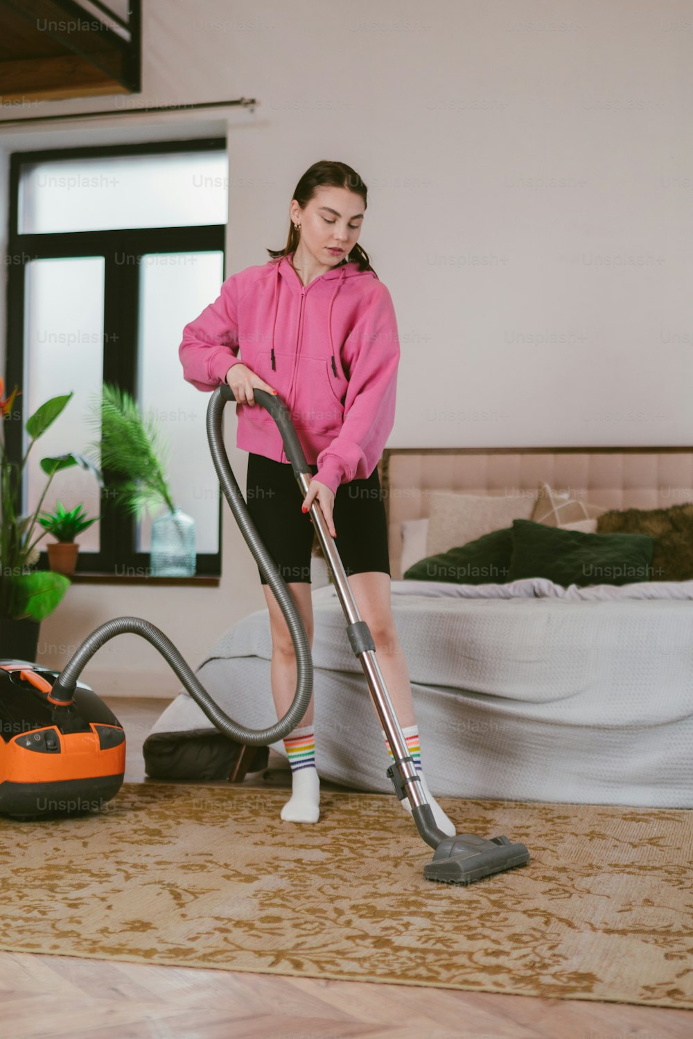 a woman in a pink hoodie is using a vacuum cleaner