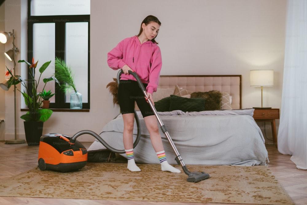 a woman in a pink shirt vacuuming a bed