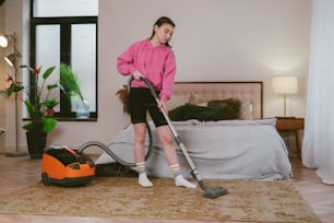 a woman in a pink shirt vacuuming a bed