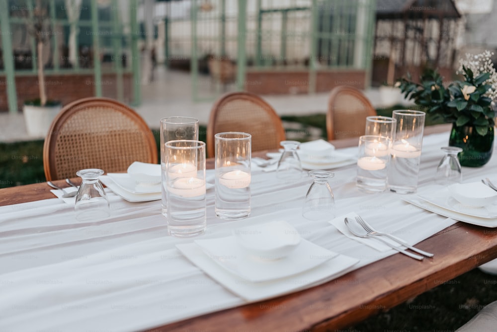 a wooden table topped with white plates and glasses