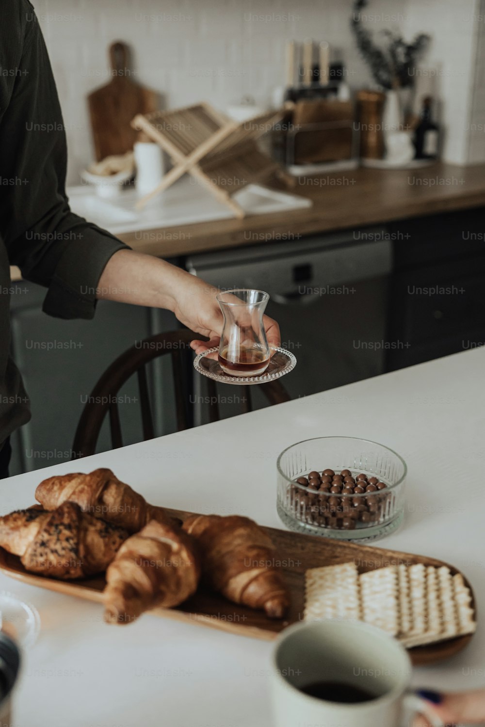 Una mujer vierte una taza de café sobre un plato de croissants
