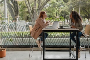 two women sitting at a table with a laptop