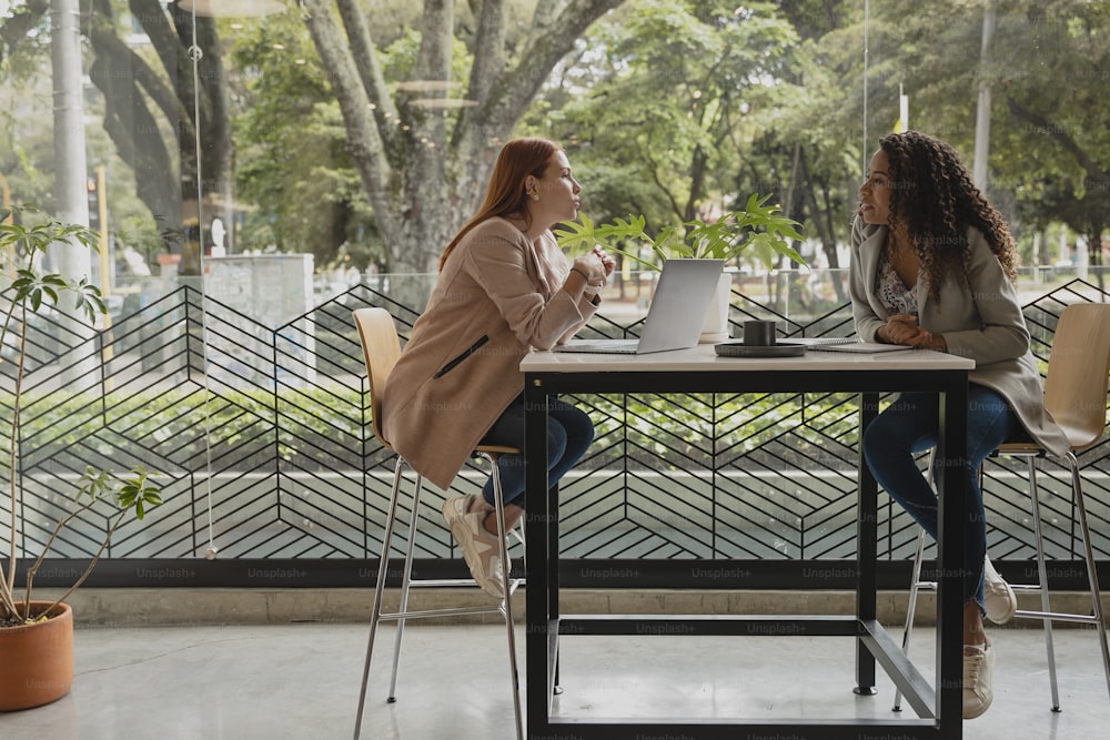 two women sitting at a table with a laptop