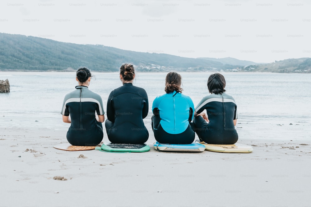 three people sitting on surfboards on a beach
