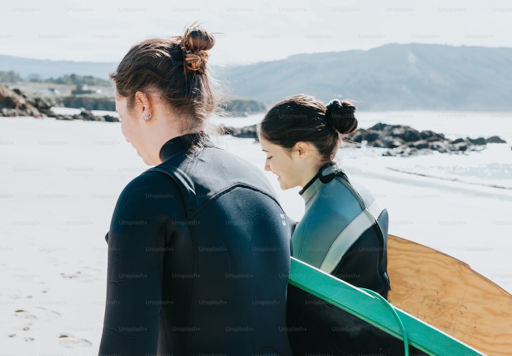 two women in wetsuits carrying surfboards on the beach