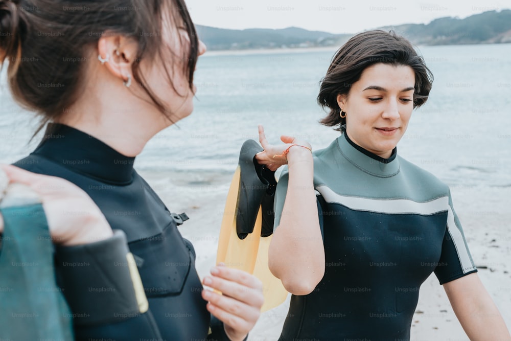 two women in wetsuits standing on a beach