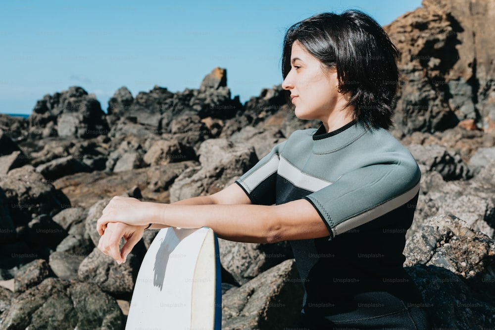 a woman sitting on rocks holding a surfboard
