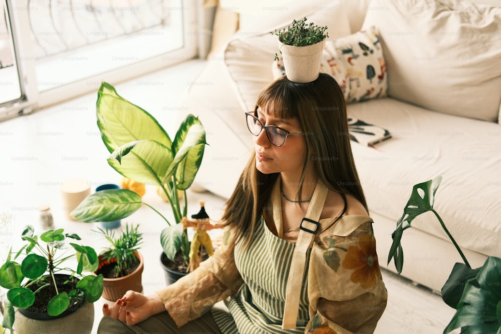 a woman sitting on the floor with a potted plant on her head