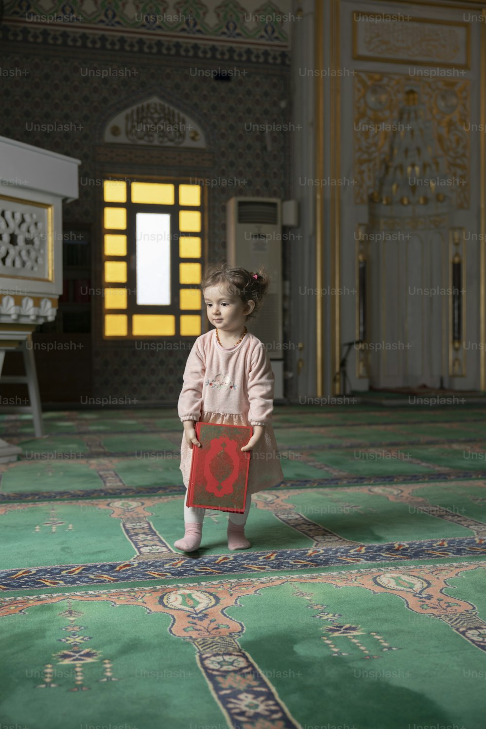 a little girl standing on a rug holding a red object