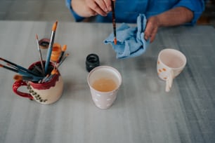 a person painting on a table next to a cup of tea