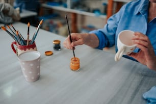 a person sitting at a table with a cup and paint brushes