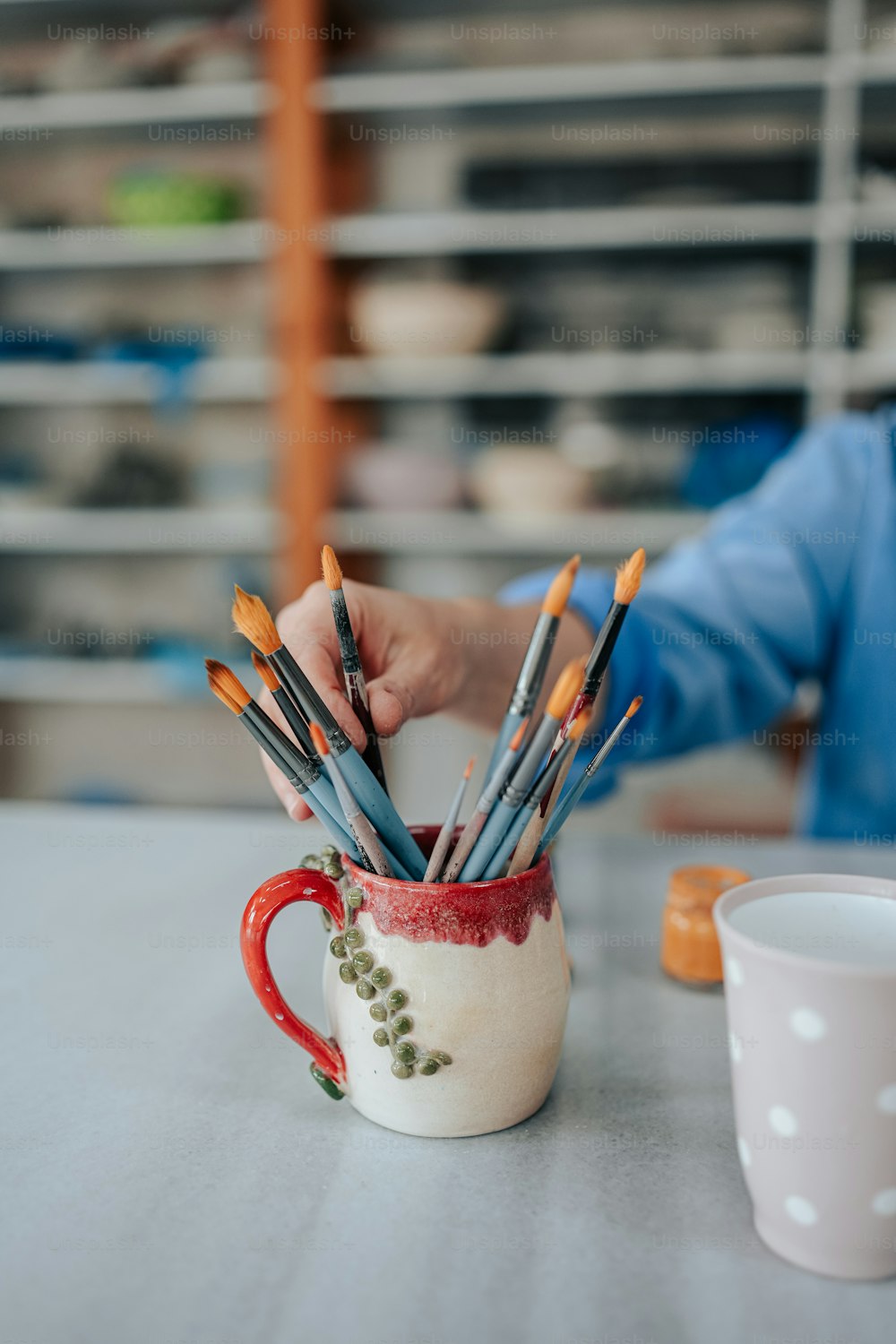 a person holding a cup with paint brushes in it