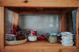 a shelf filled with cups and bowls on top of a wooden shelf