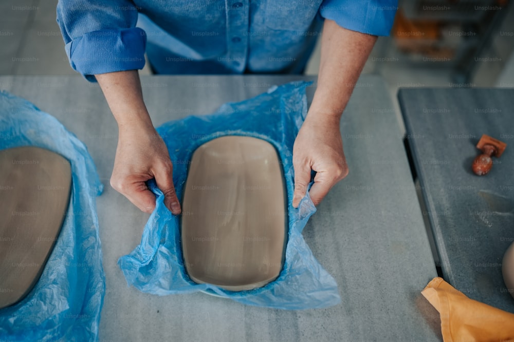 Une personne en chemise bleue fabrique un morceau de poterie