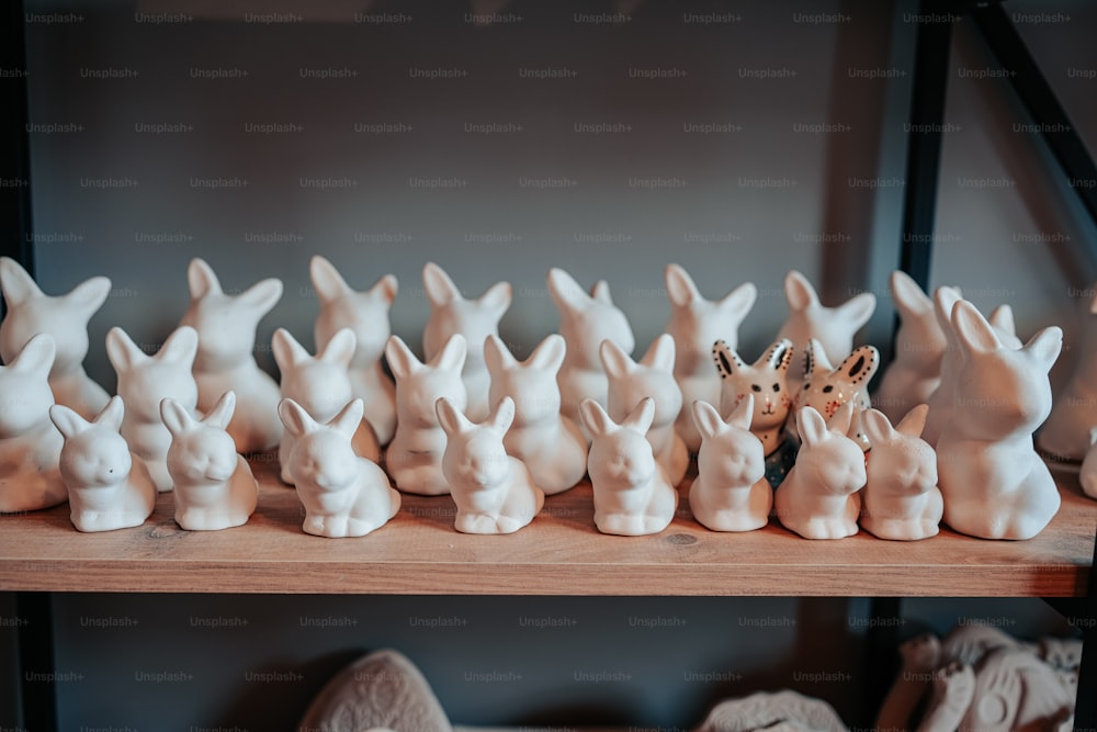 a shelf filled with white ceramic rabbits on top of a wooden shelf