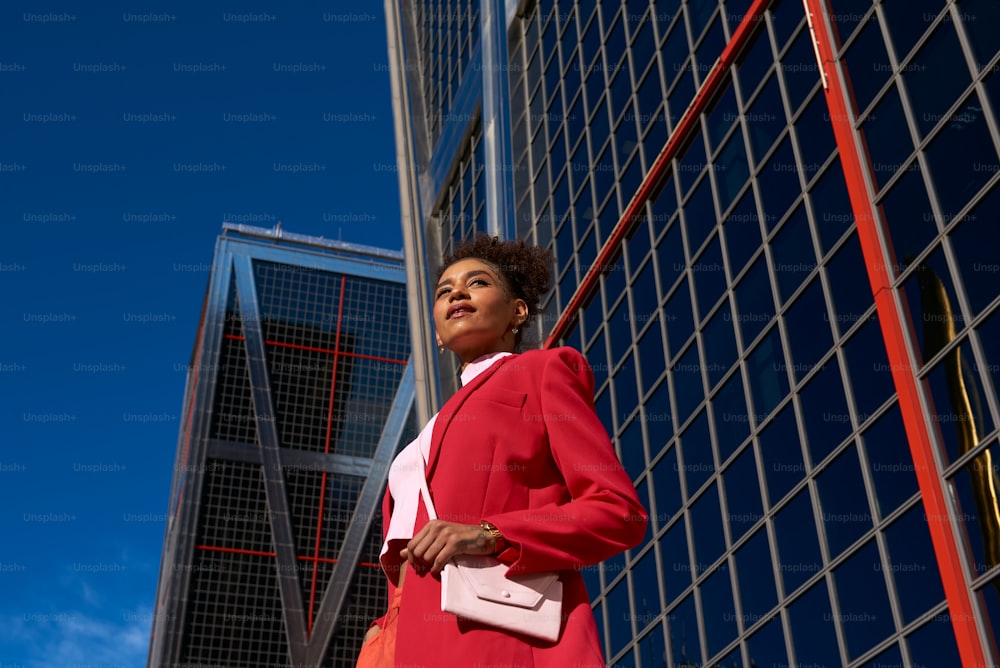 a woman in a red suit standing in front of a tall building
