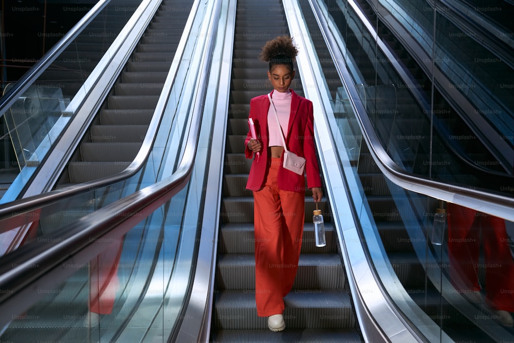 a woman in a red suit is going down an escalator
