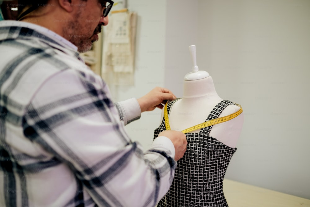 a man measuring a dress on a mannequin