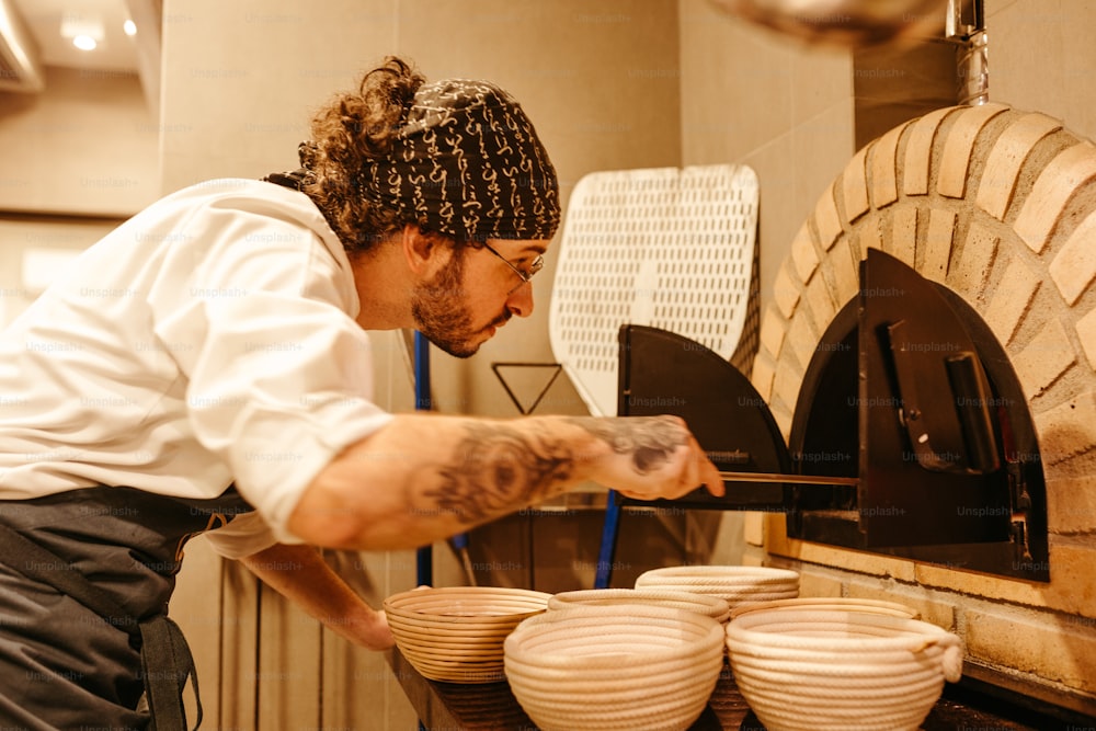 um homem em uniforme de chef está colocando comida em um forno de pizza