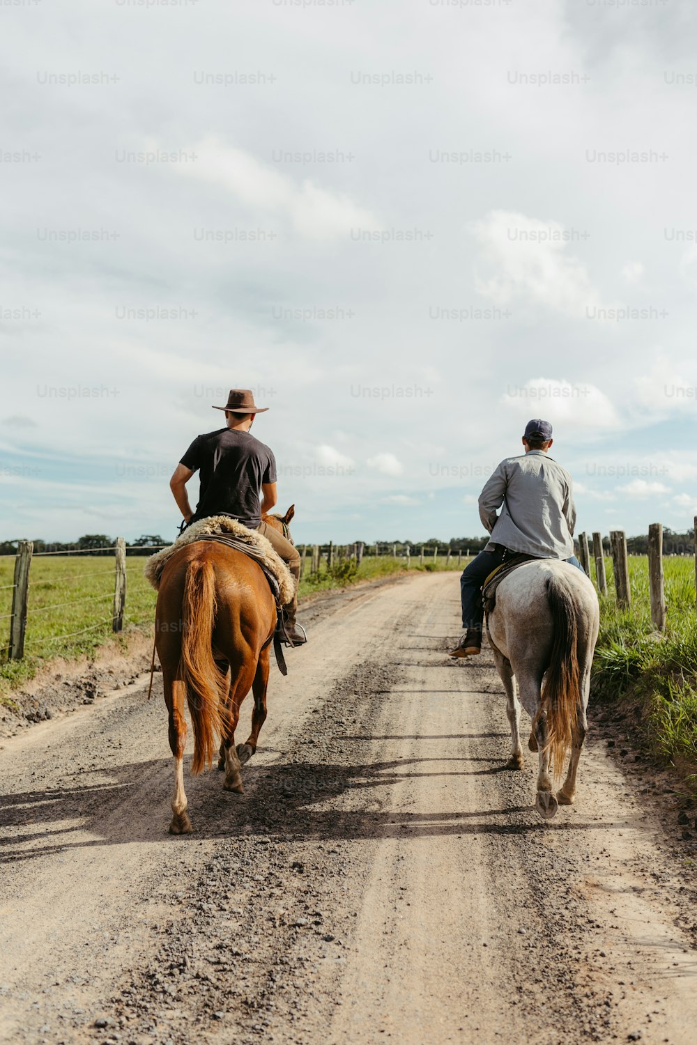 two men riding horses down a dirt road