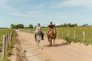 two people riding horses down a dirt road