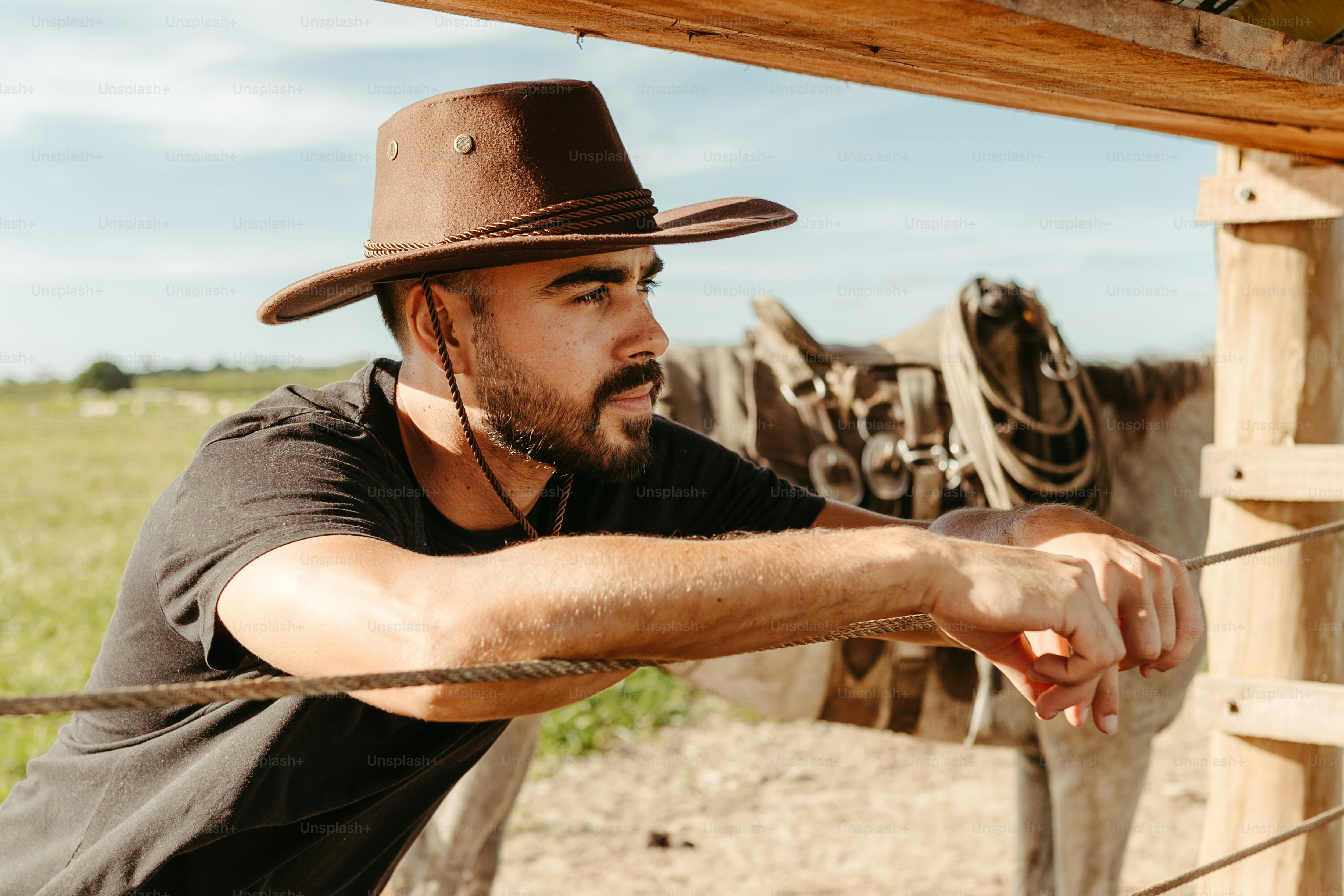 a man in a cowboy hat leaning on a fence