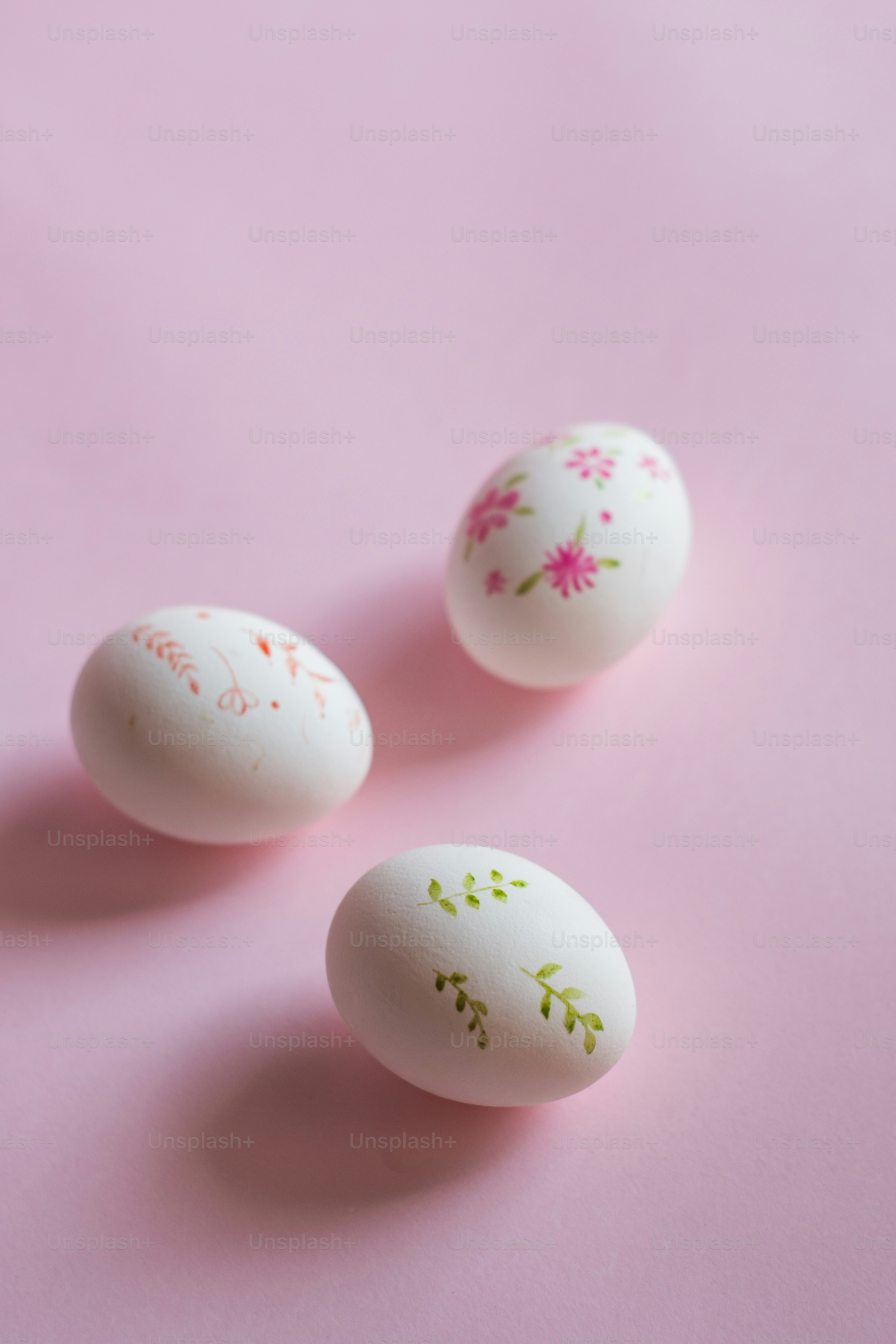 Tres huevos decorados sentados encima de una superficie rosa