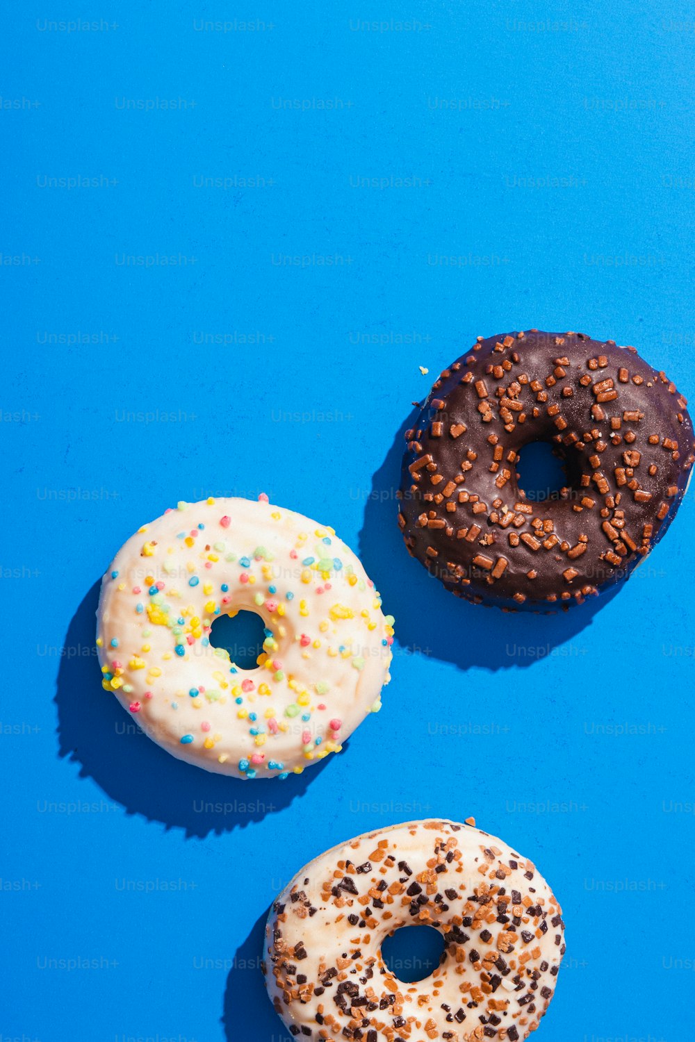 three donuts with sprinkles on a blue surface