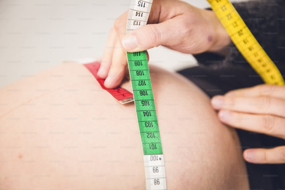 a person measuring a pregnant belly with a measuring tape