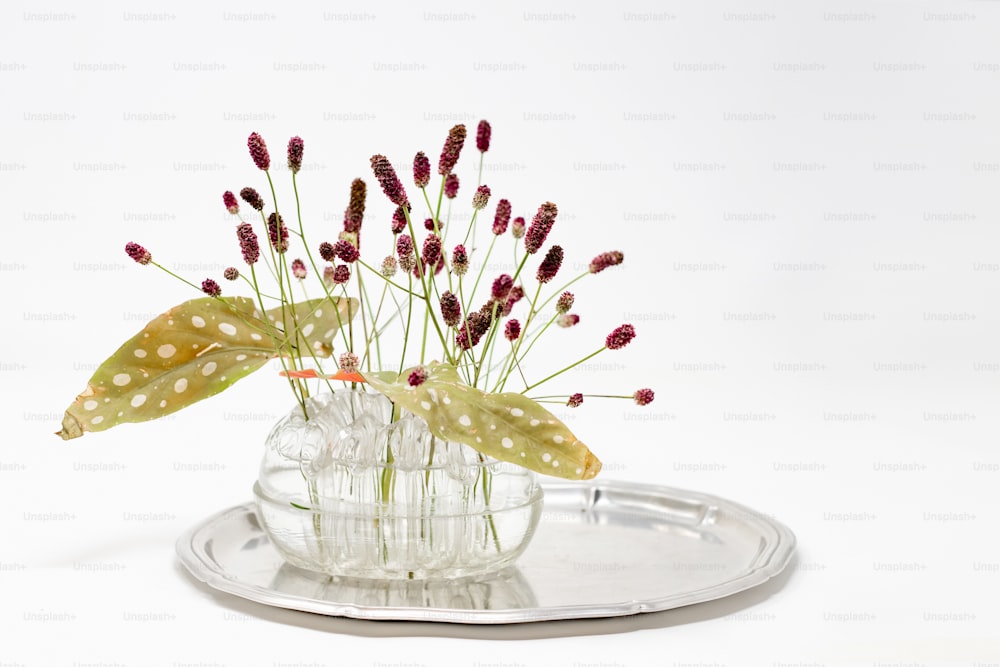 un jarrón de vidrio lleno de flores encima de una bandeja de metal
