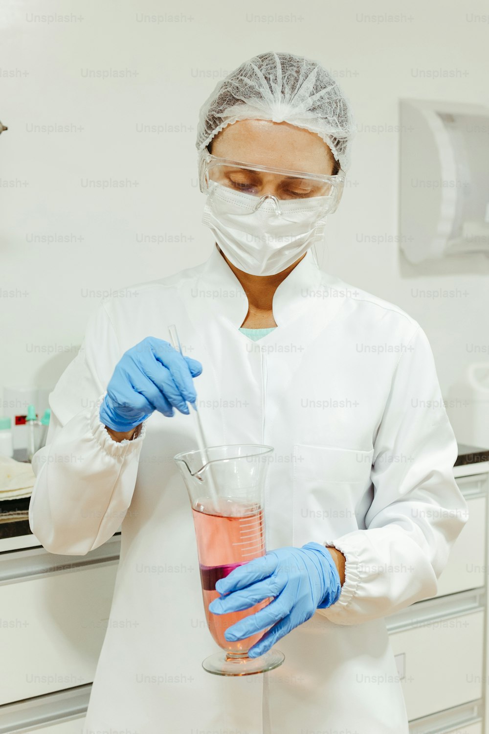 a person in a white coat and blue gloves holding a beaker
