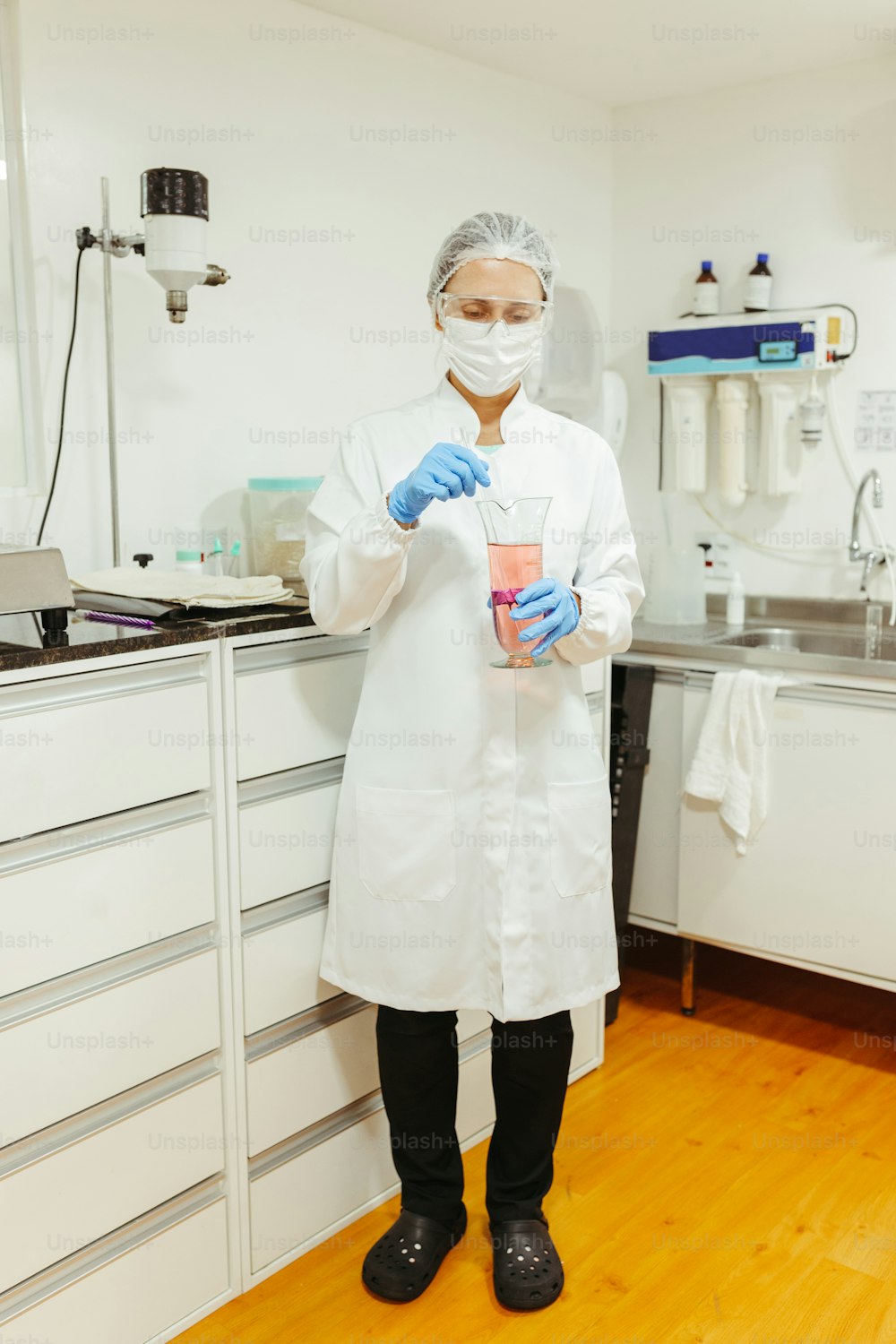 실험실 코트와 마��스크를 쓴 사람이 컵을 들고 있다