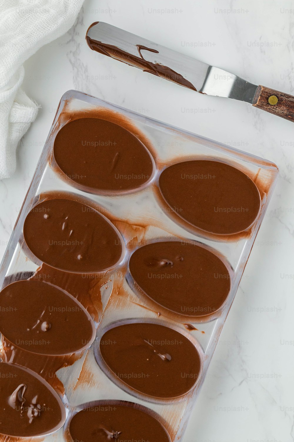ein Tablett mit mit Schokolade überzogenen Cupcakes neben einem Messer