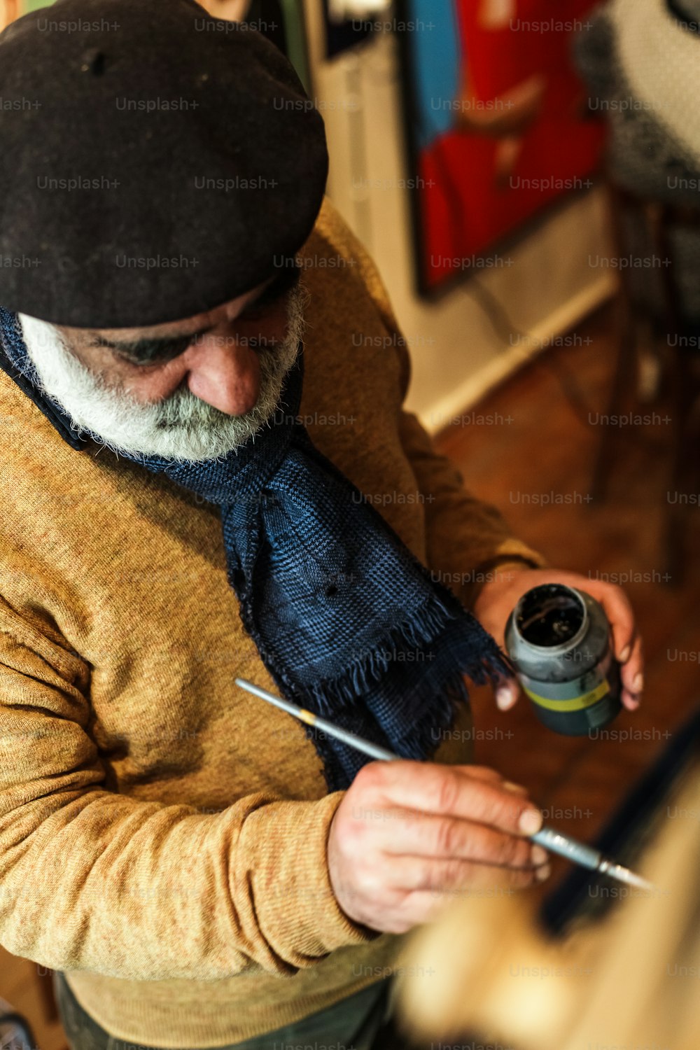 a man with a hat and scarf is painting a picture