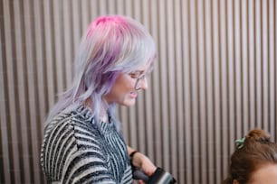 a woman with pink hair is blow drying another woman's hair