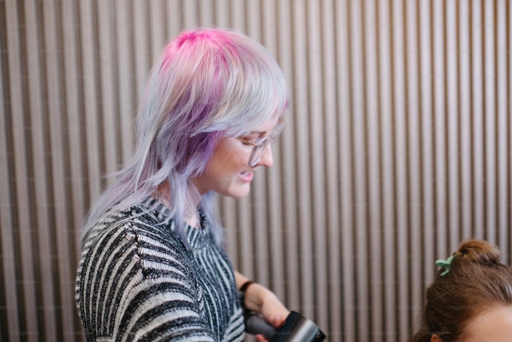 a woman with pink hair is blow drying another woman's hair
