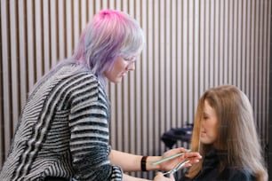 a woman getting her hair cut by a woman with pink hair