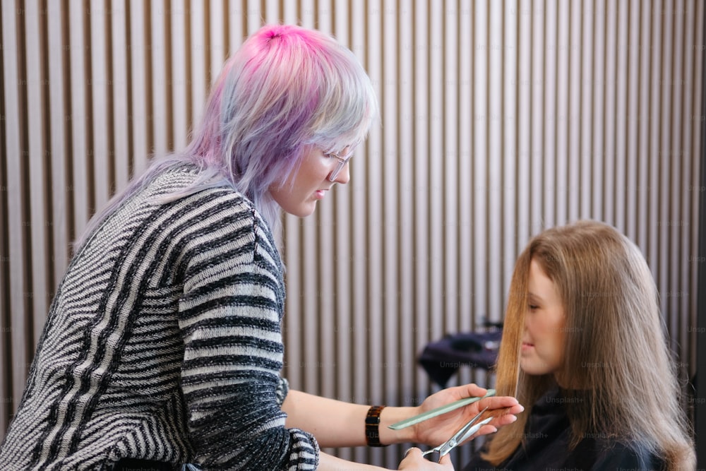 a woman getting her hair cut by a woman with pink hair