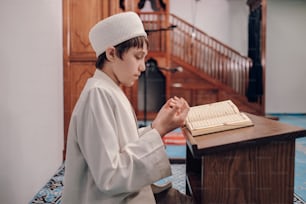a young boy in a white outfit sitting at a table with an open book