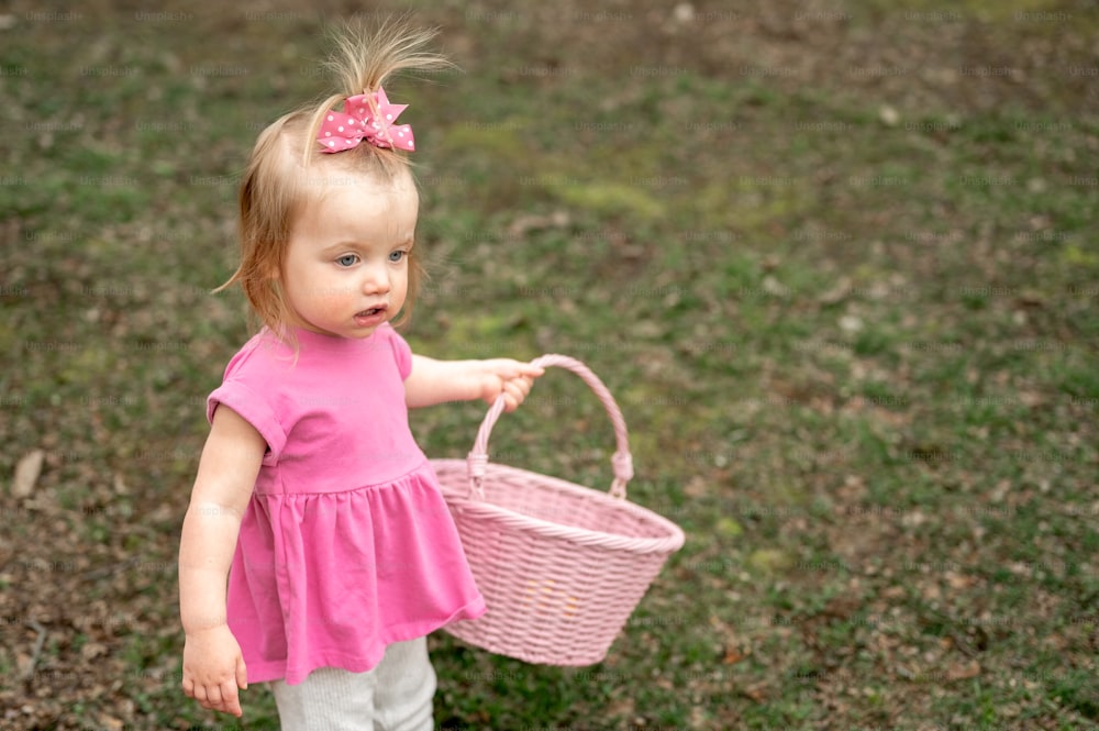 a little girl holding a pink basket in a field