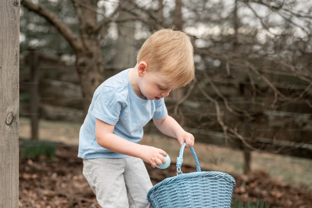 a young boy holding a blue basket in a yard