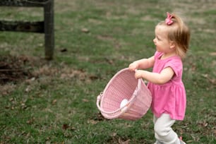 a little girl holding a pink basket in a field