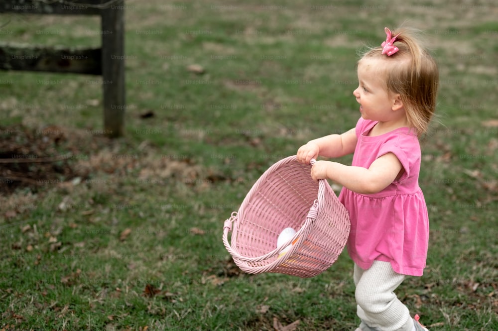 a little girl holding a pink basket in a field