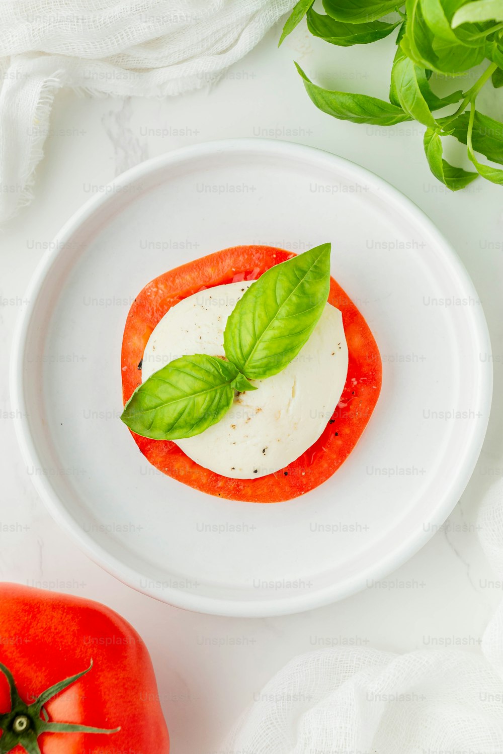 une assiette blanche garnie d’une tomate et de basilic