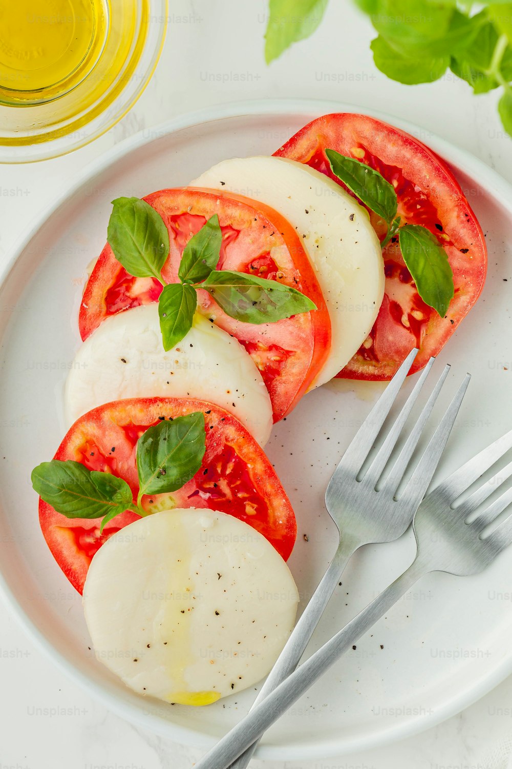 um prato branco coberto com tomates fatiados e manjericão