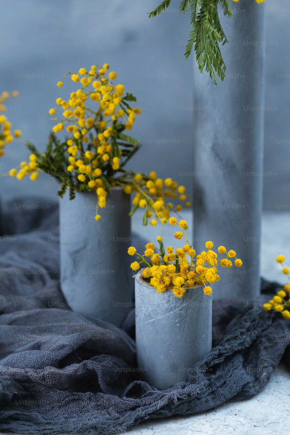 Tres jarrones de cemento con flores amarillas en ellos