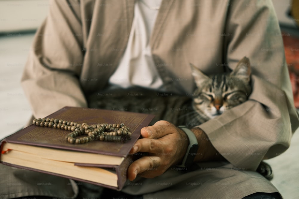a man holding a book with a cat sitting on top of it